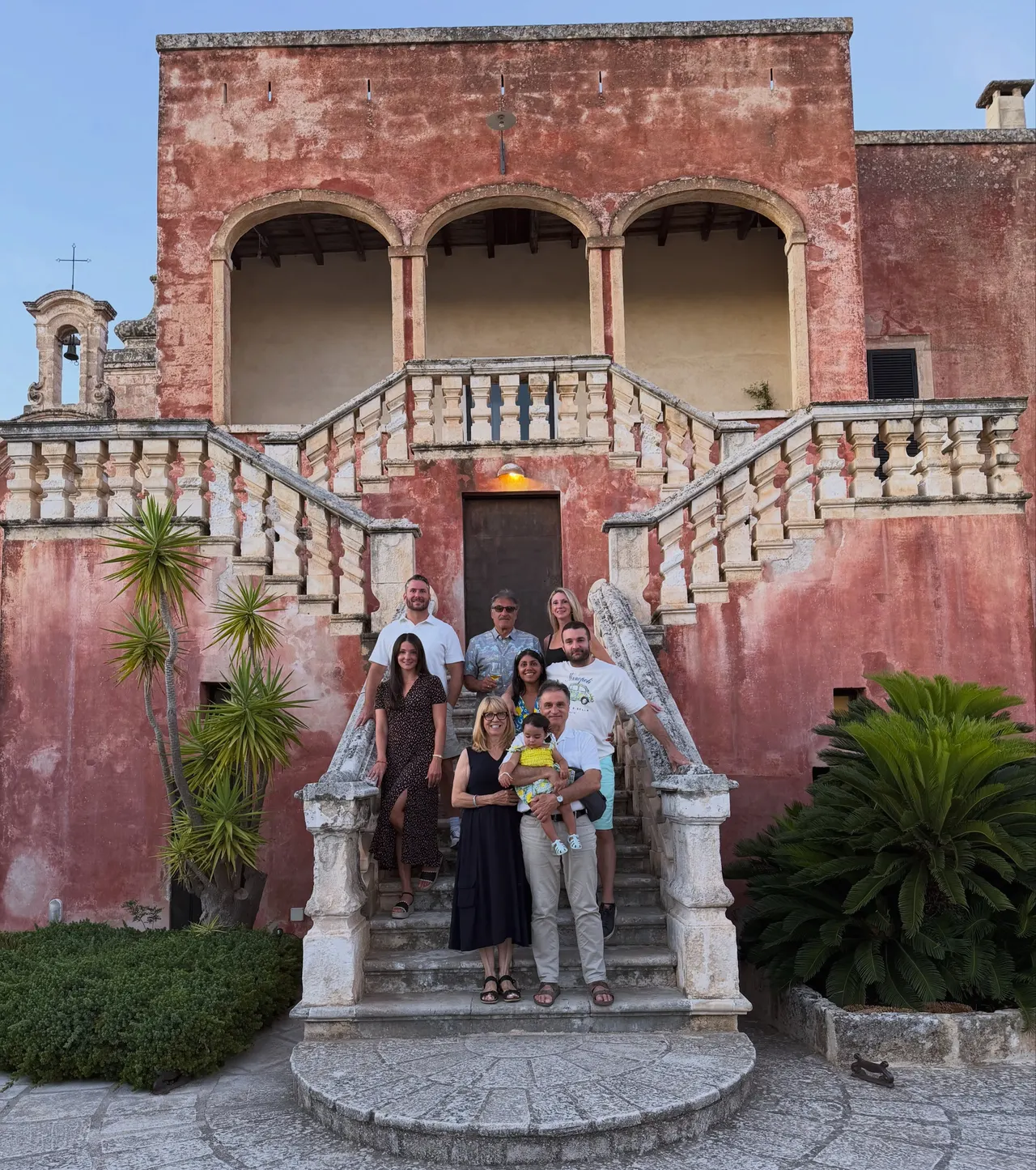 Extended family gathered on the pink staircase of a masseria at dusk