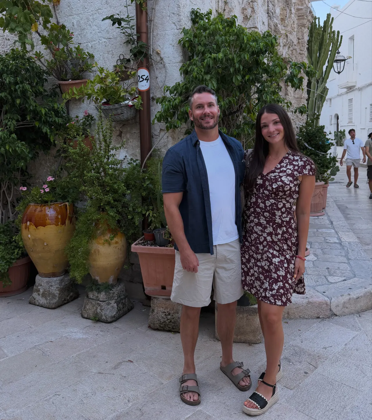 Drew and Valerie standing in a whitewashed lane beside potted plants