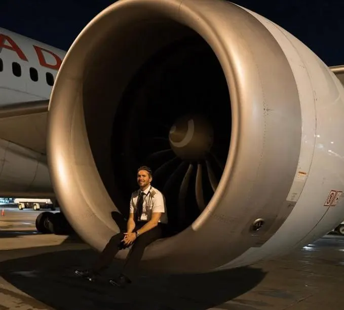 Drew in his pilot uniform sitting inside a jet engine intake at night